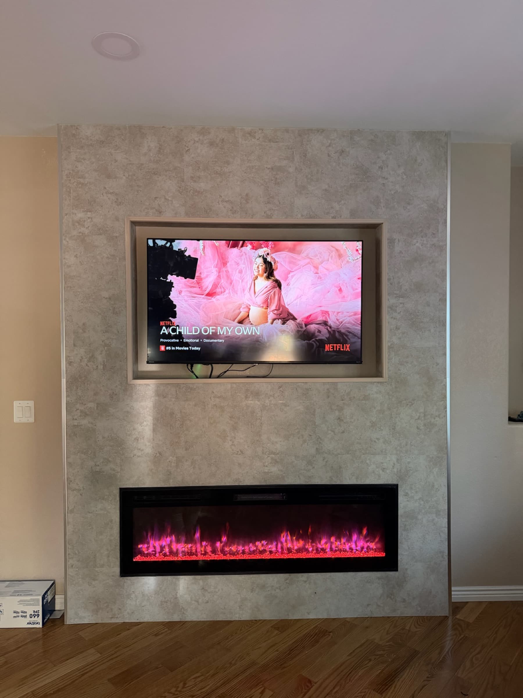 Completed custom media wall with recessed TV niche and linear electric fireplace, stone tile finish